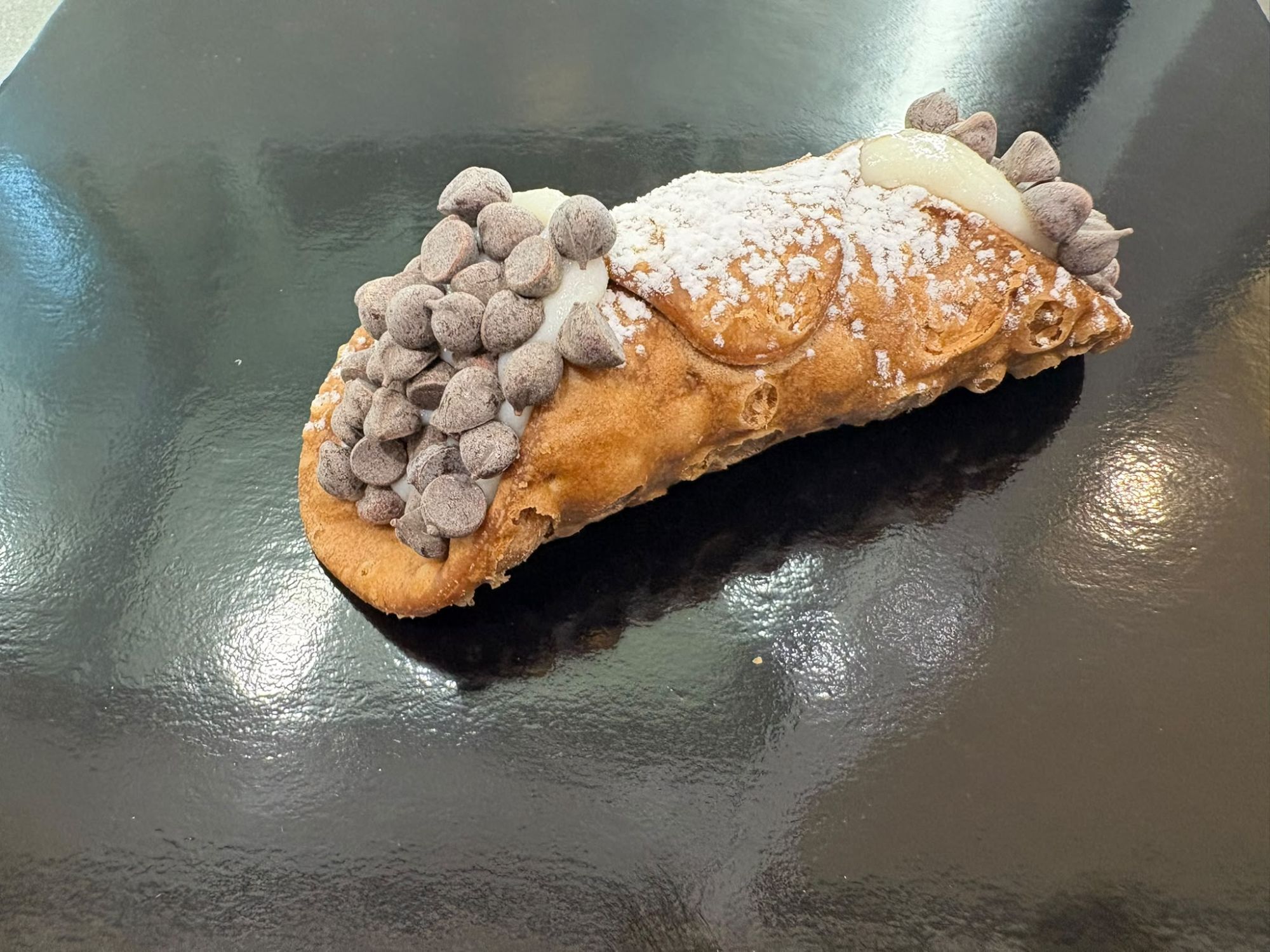 Cannolo farcito con crema e gocce di cioccolato, spolverato di zucchero a velo