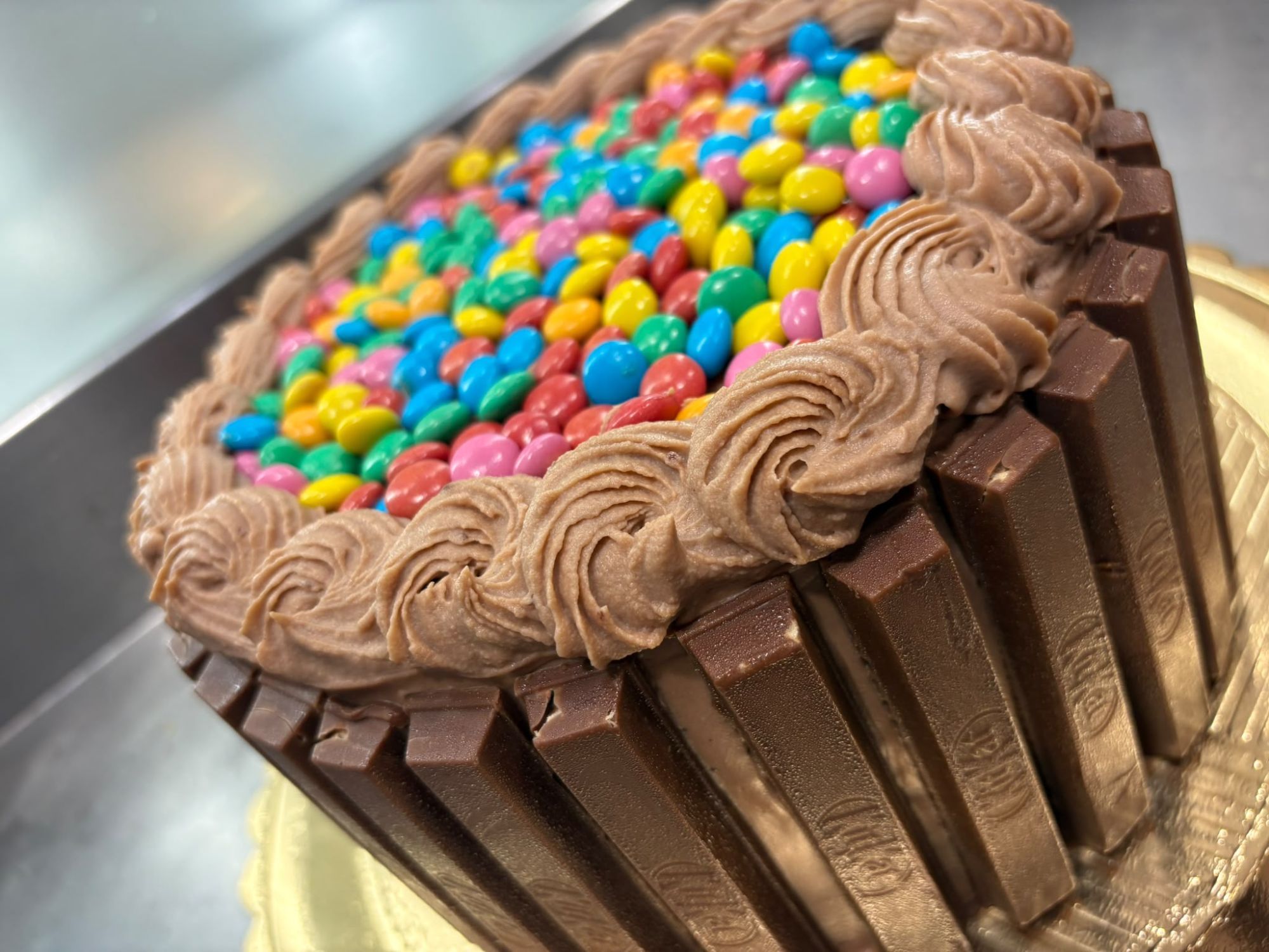 Torta al cioccolato con ciuffi di crema, bordo di barrette di cioccolato e confettini colorati sopra
